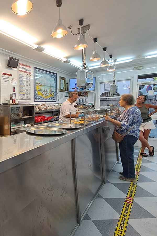 Inside Reina Victoria Pescaderia y Freiduria in Triana Seville. One woamn is being served, andother is waiting in line for fried fish.