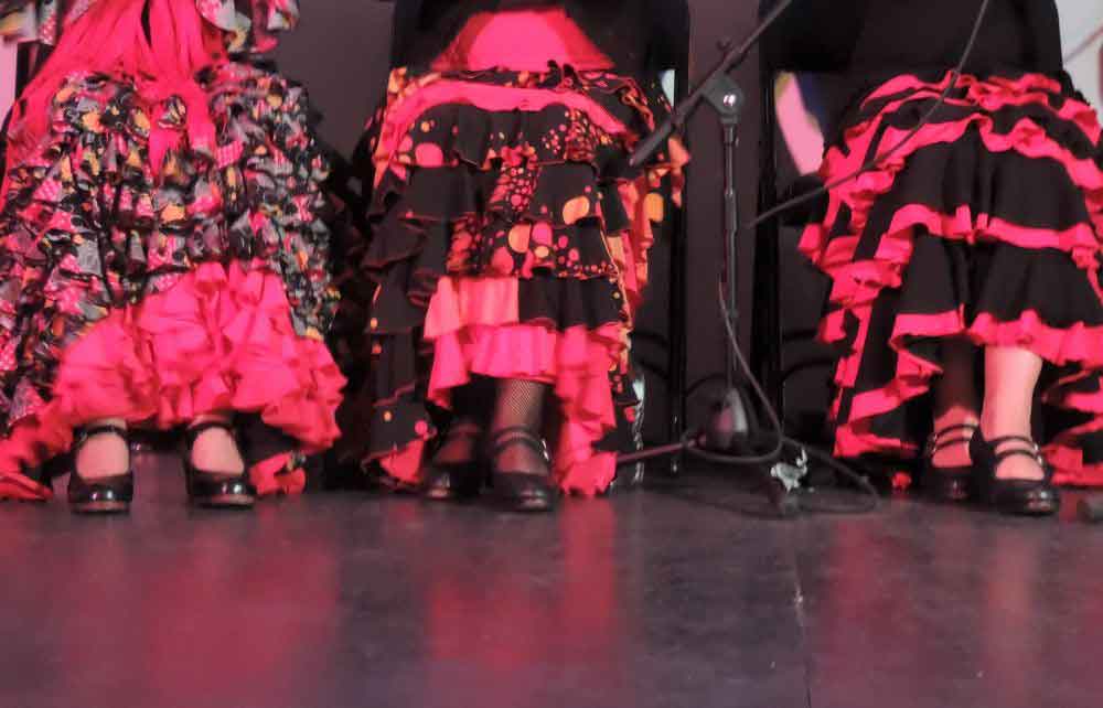Flamenco cosutumes The dresses and feet of three ladies sat on chairs during a flamenco show.