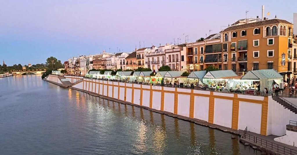 Velá de Santa Ana Seville with casetas reflecting in the river at dusk featured image